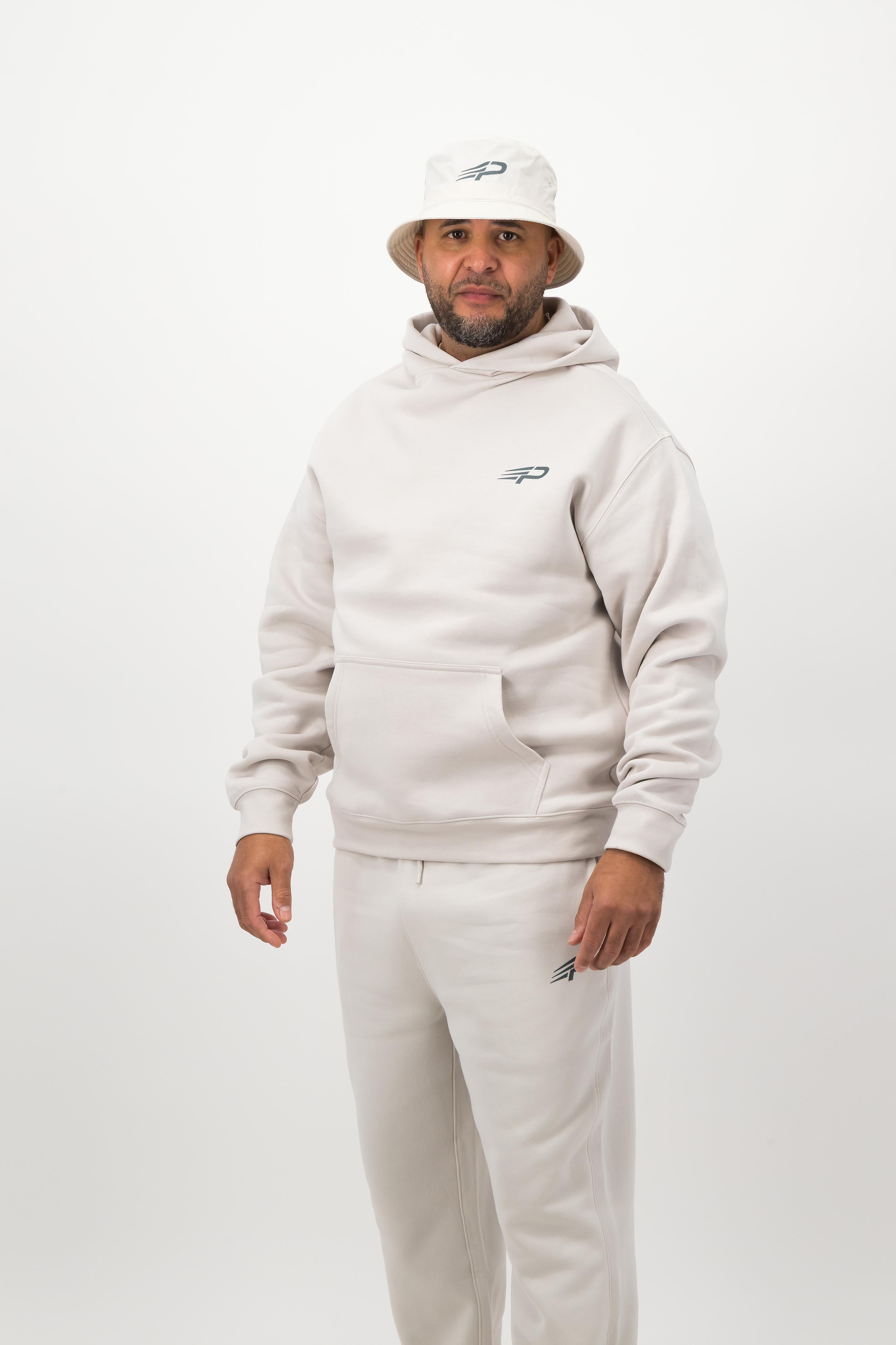 Person wearing a light hoodie, sweatpants and a bucket hat posing against a white background