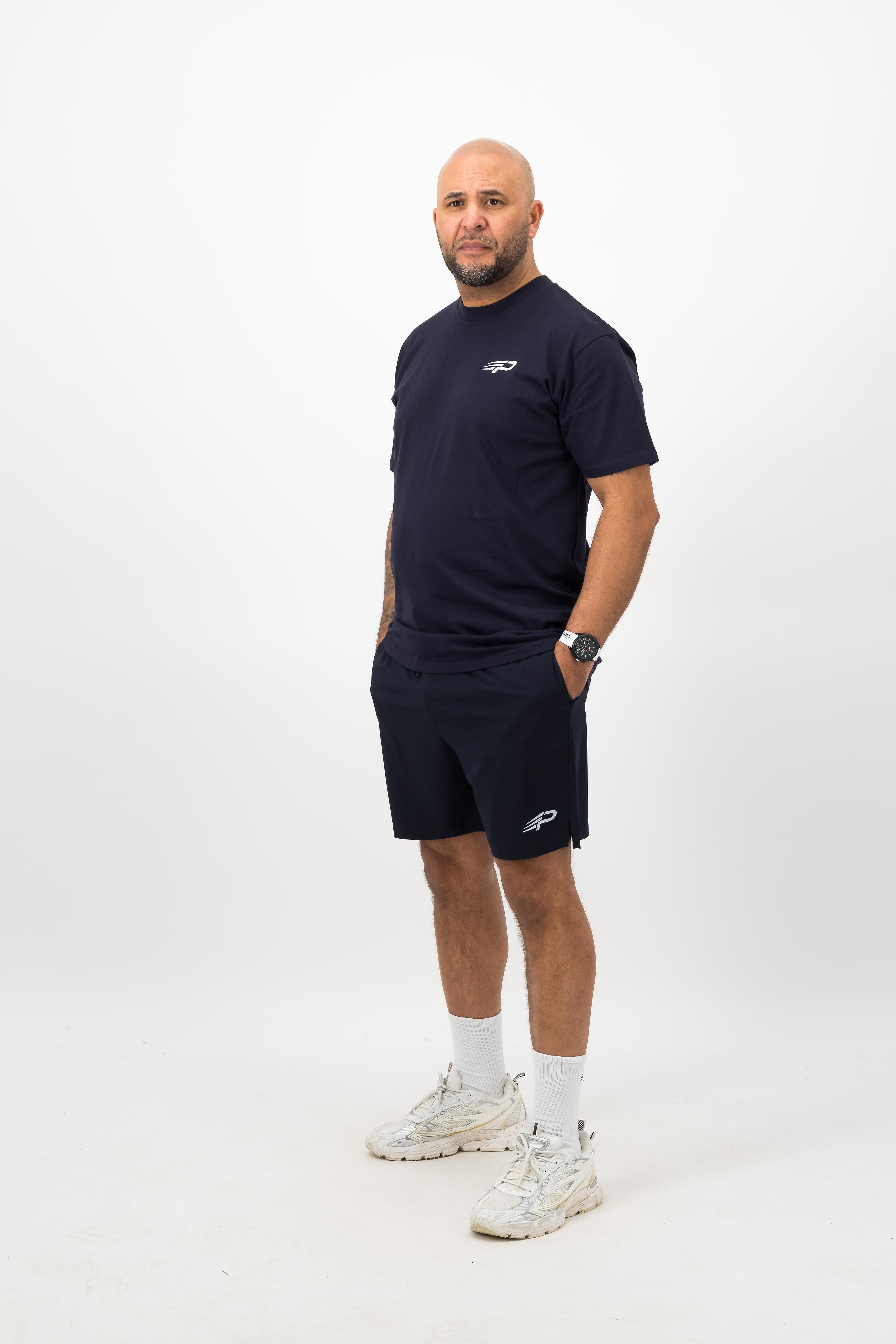 Person wearing a Concept Padel ink blue rebound tee standing side on, paired with matching shorts and trainers against a white background