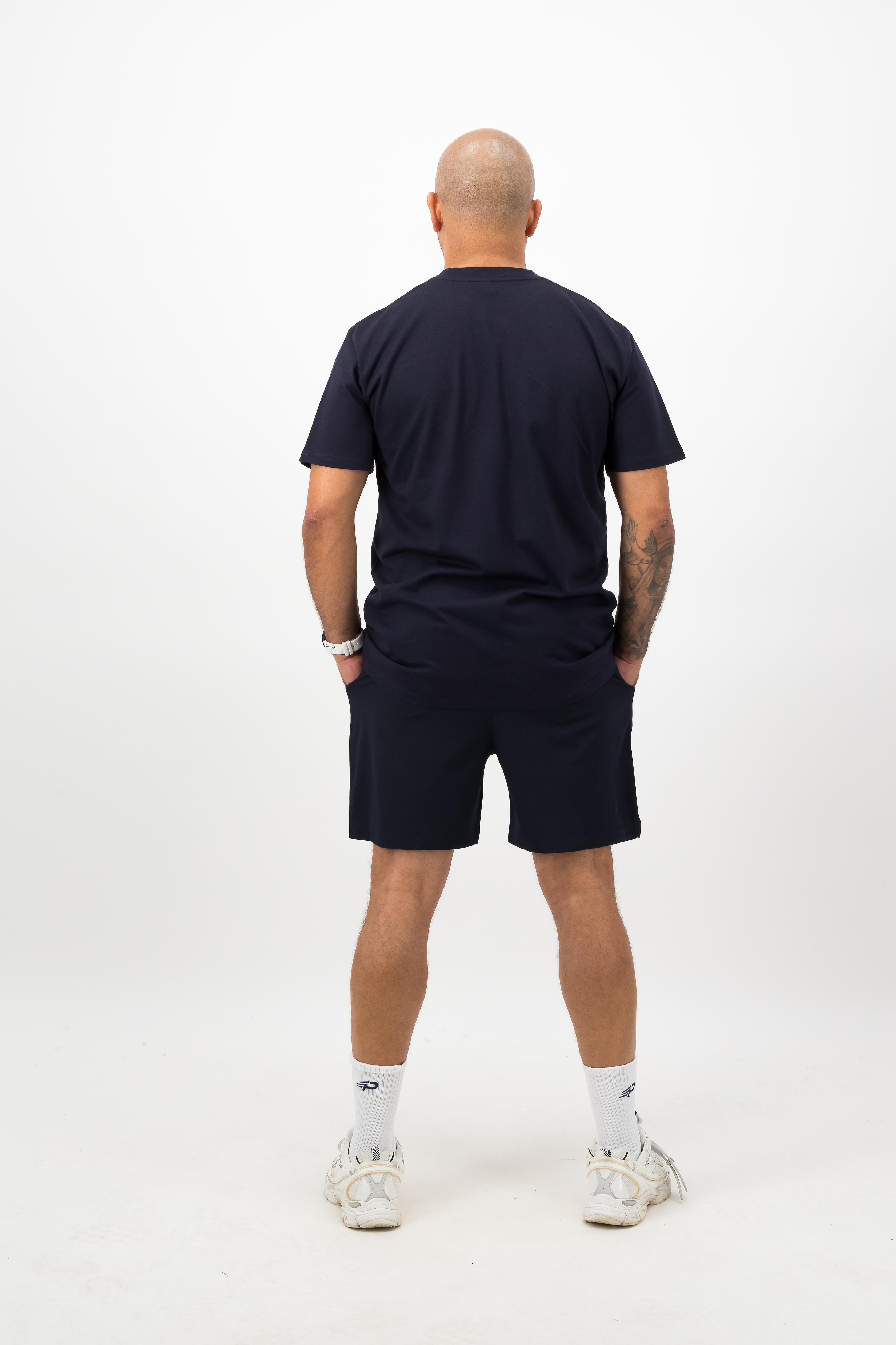 Person wearing a Concept Padel ink blue rebound tee standing with back to camera showing the clean back silhouette, styled with matching shorts and trainers against a white background