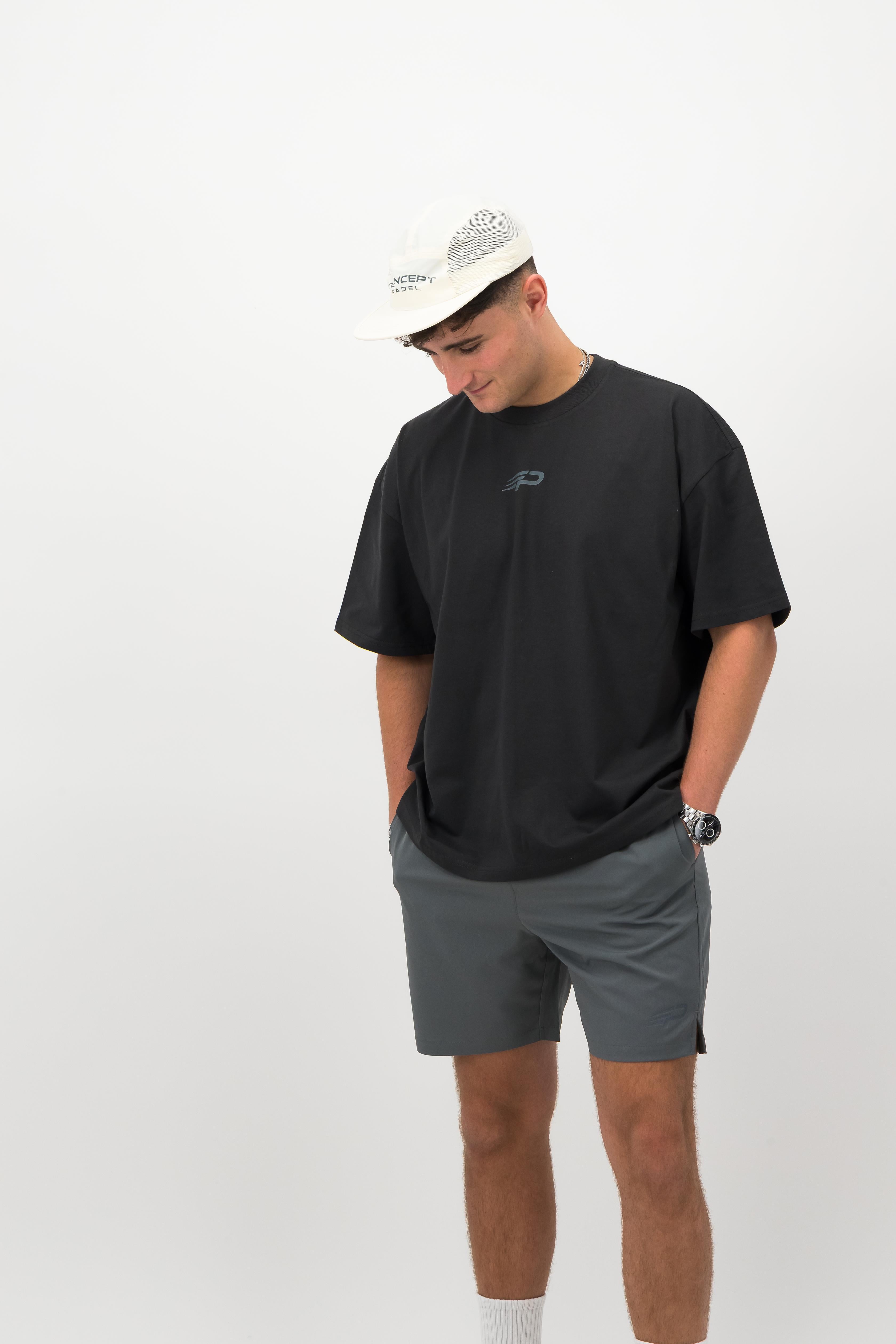 Man wearing ecru Concept Padel performance cap with black oversized T‑shirt and grey shorts front view