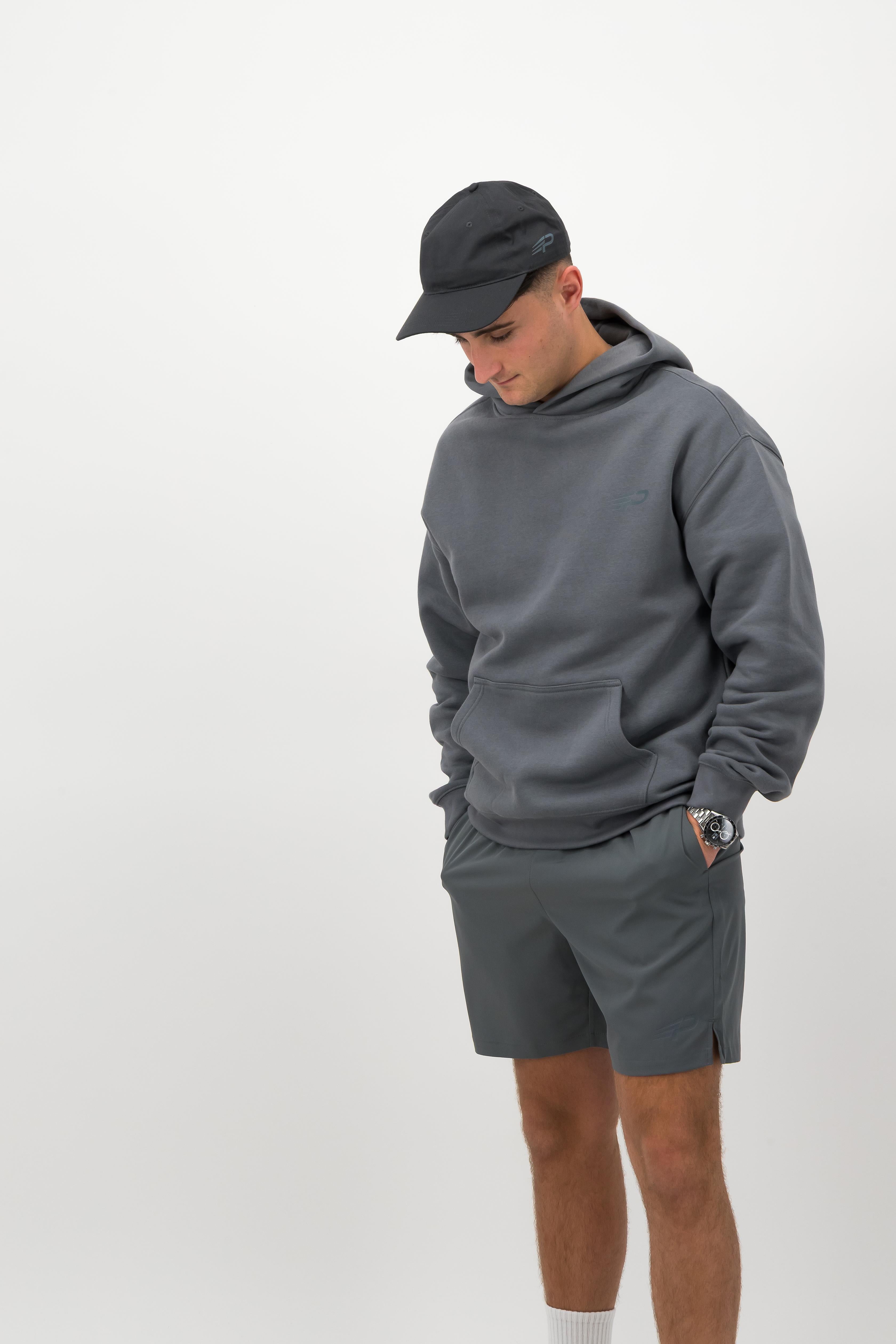 Person wearing a Concept Padel shadow rebound hoodie standing in a relaxed pose, paired with grey shorts and trainers against a white background