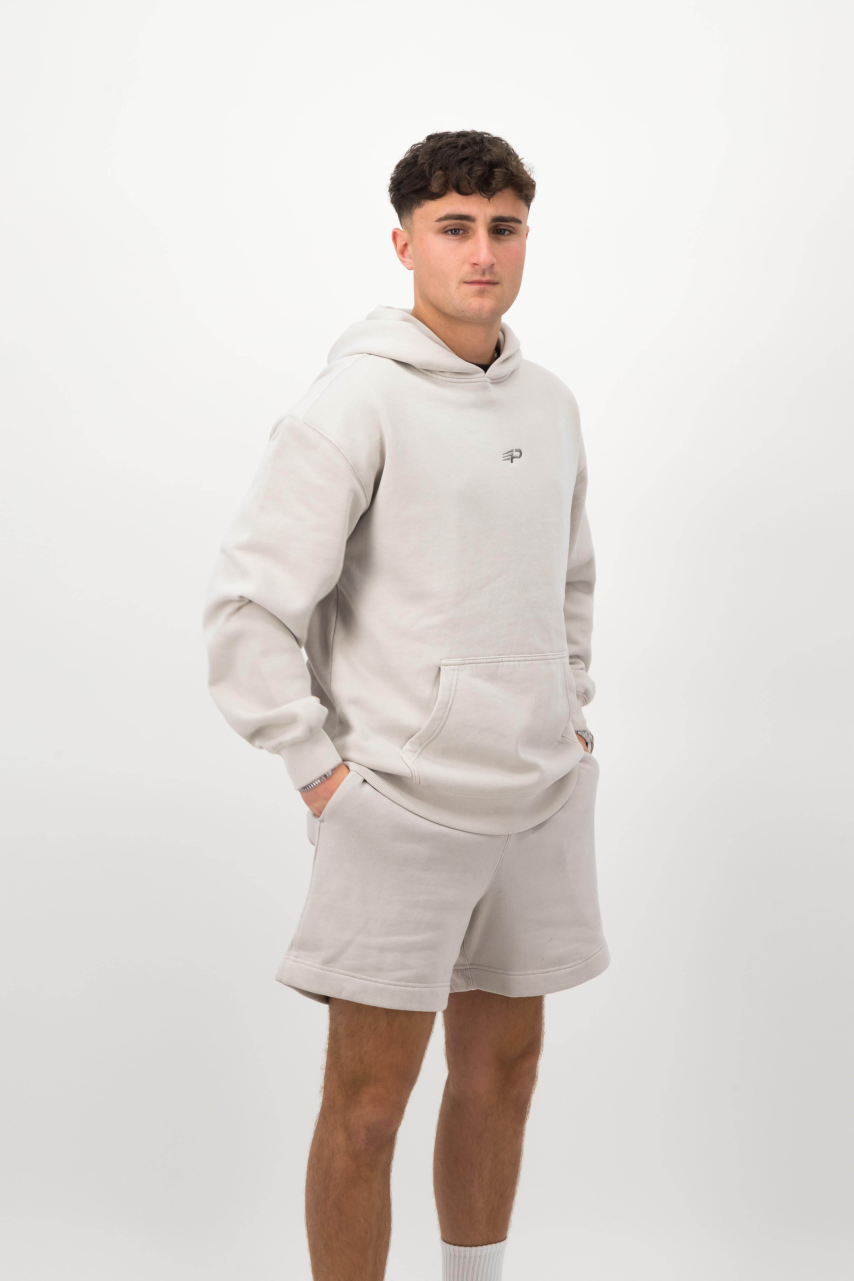 Person wearing a Concept Padel bone faded hoodie standing side on, paired with matching shorts and trainers against a white background