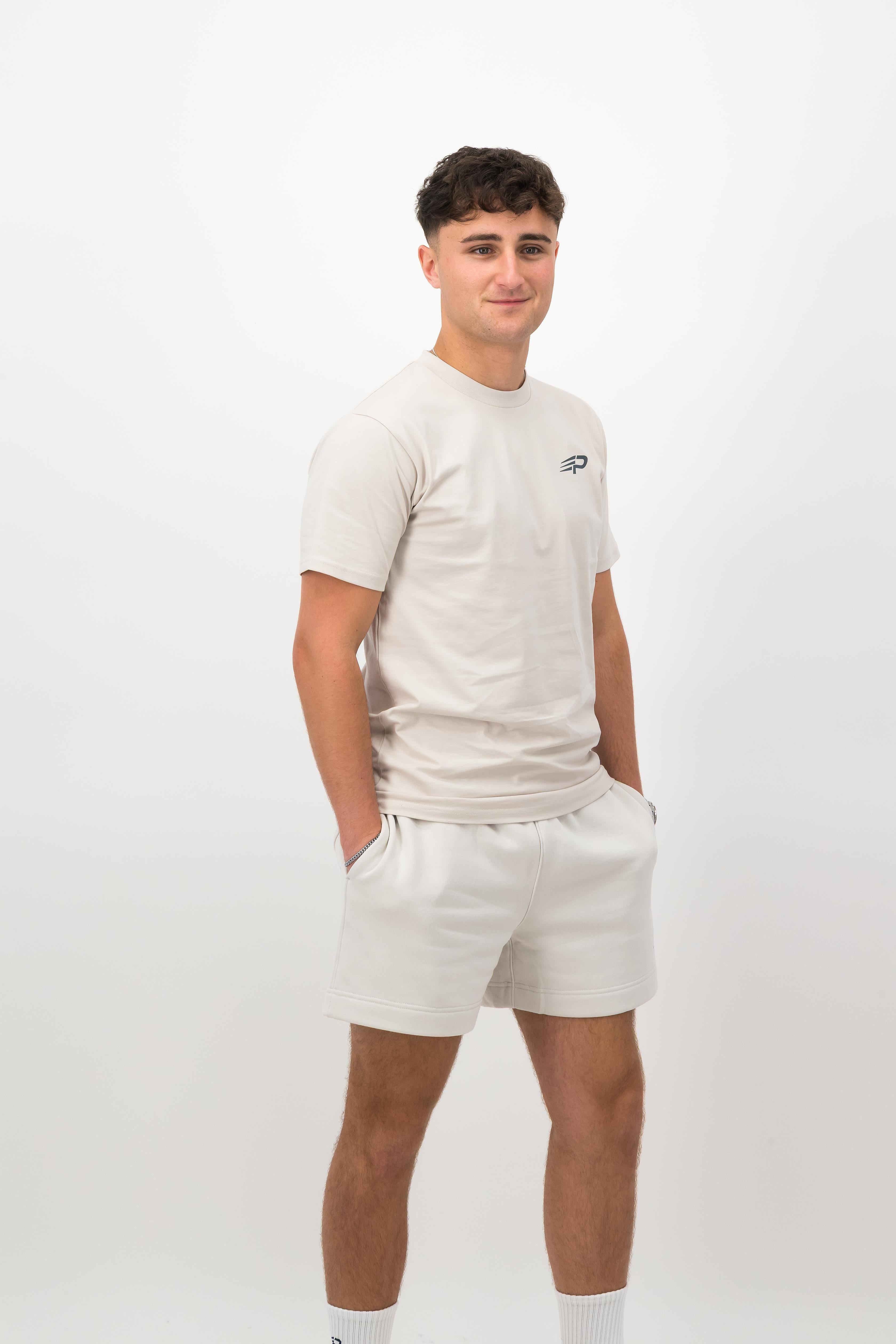 Person wearing a Concept Padel bone rebound tee standing side on, paired with white shorts and trainers against a white background