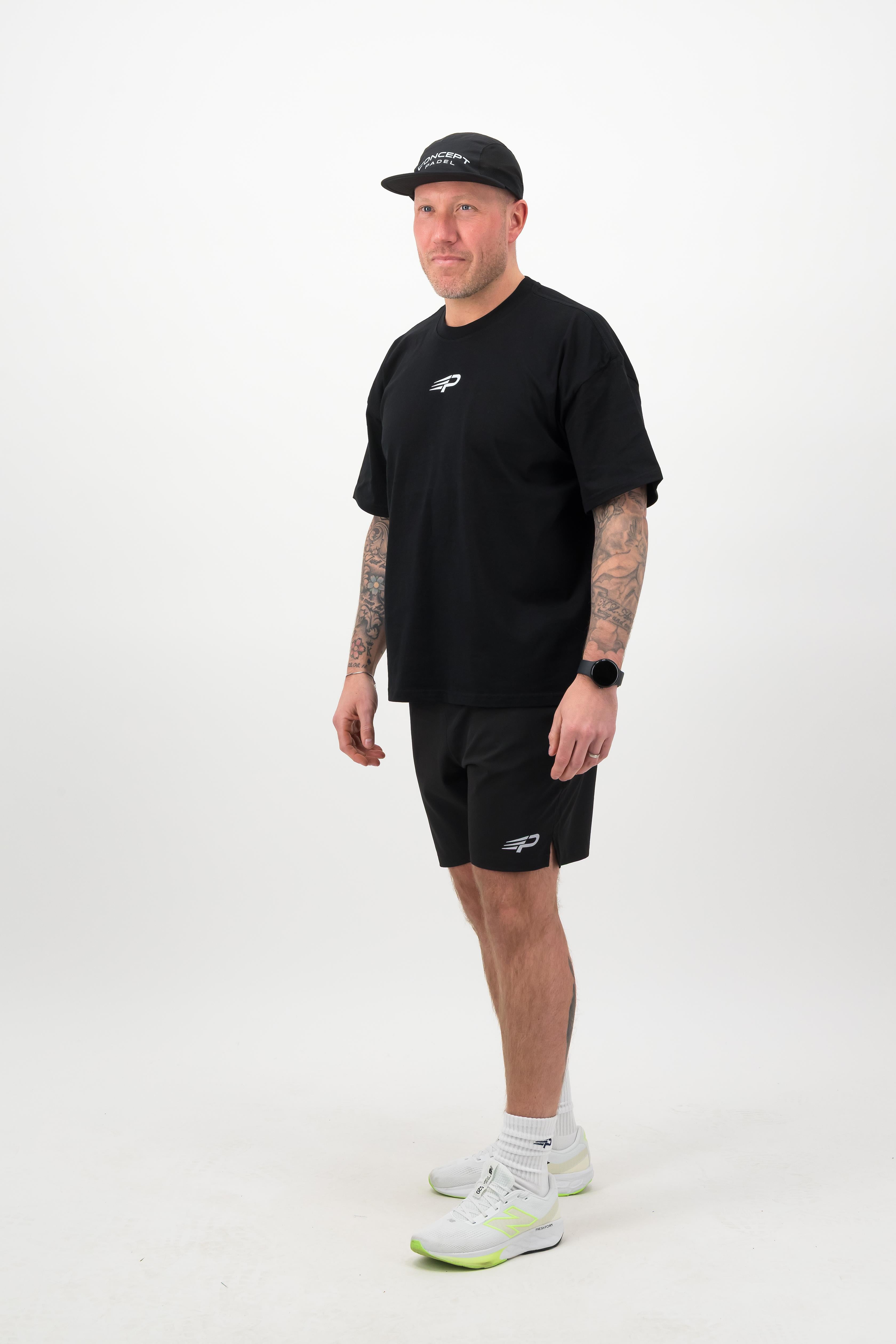 Side view of a person wearing a black T‑shirt, black shorts and a black cap against a white background
