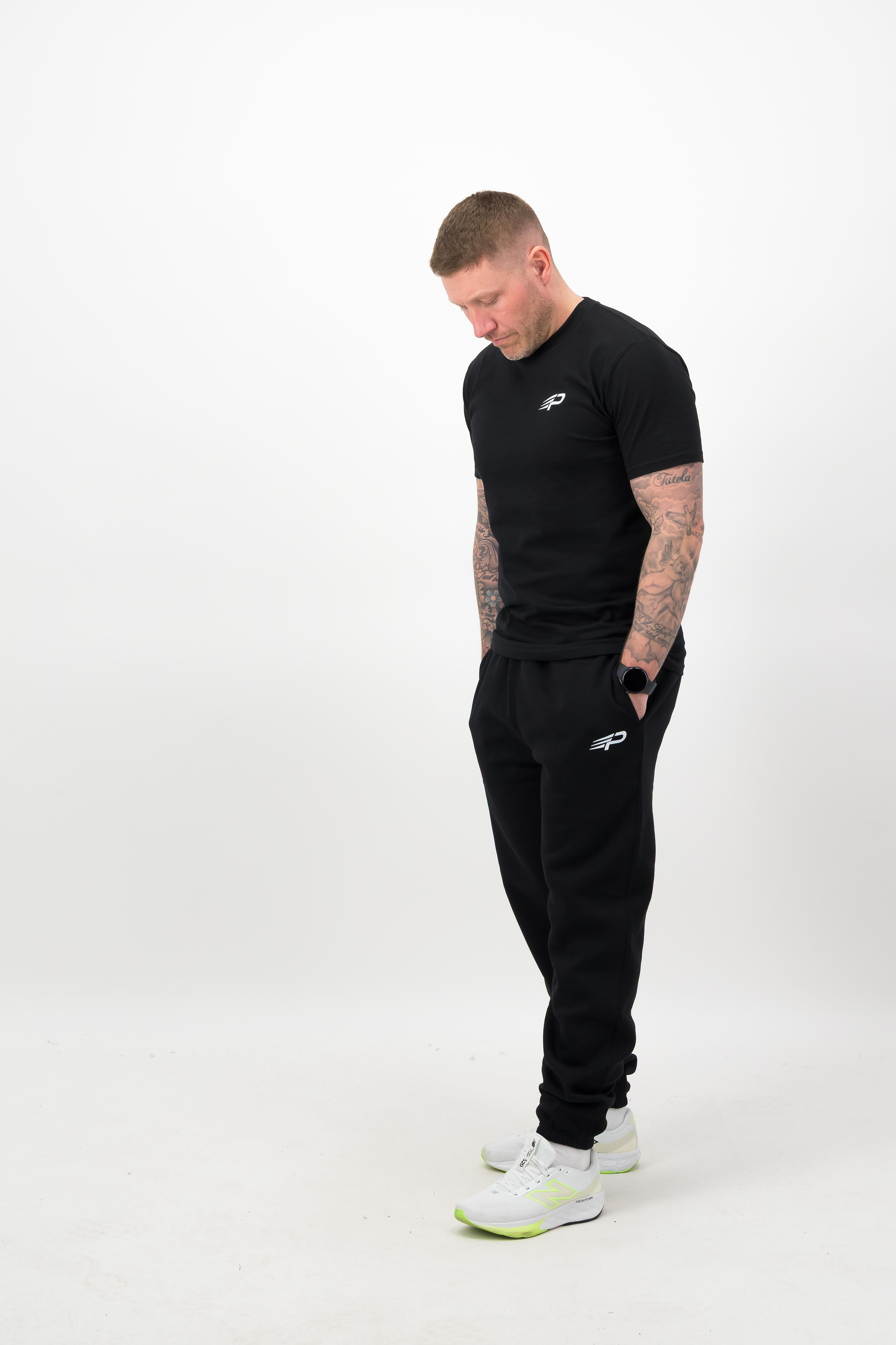 Person wearing a Concept Padel black rebound tee standing side on, paired with black joggers and trainers against a white background