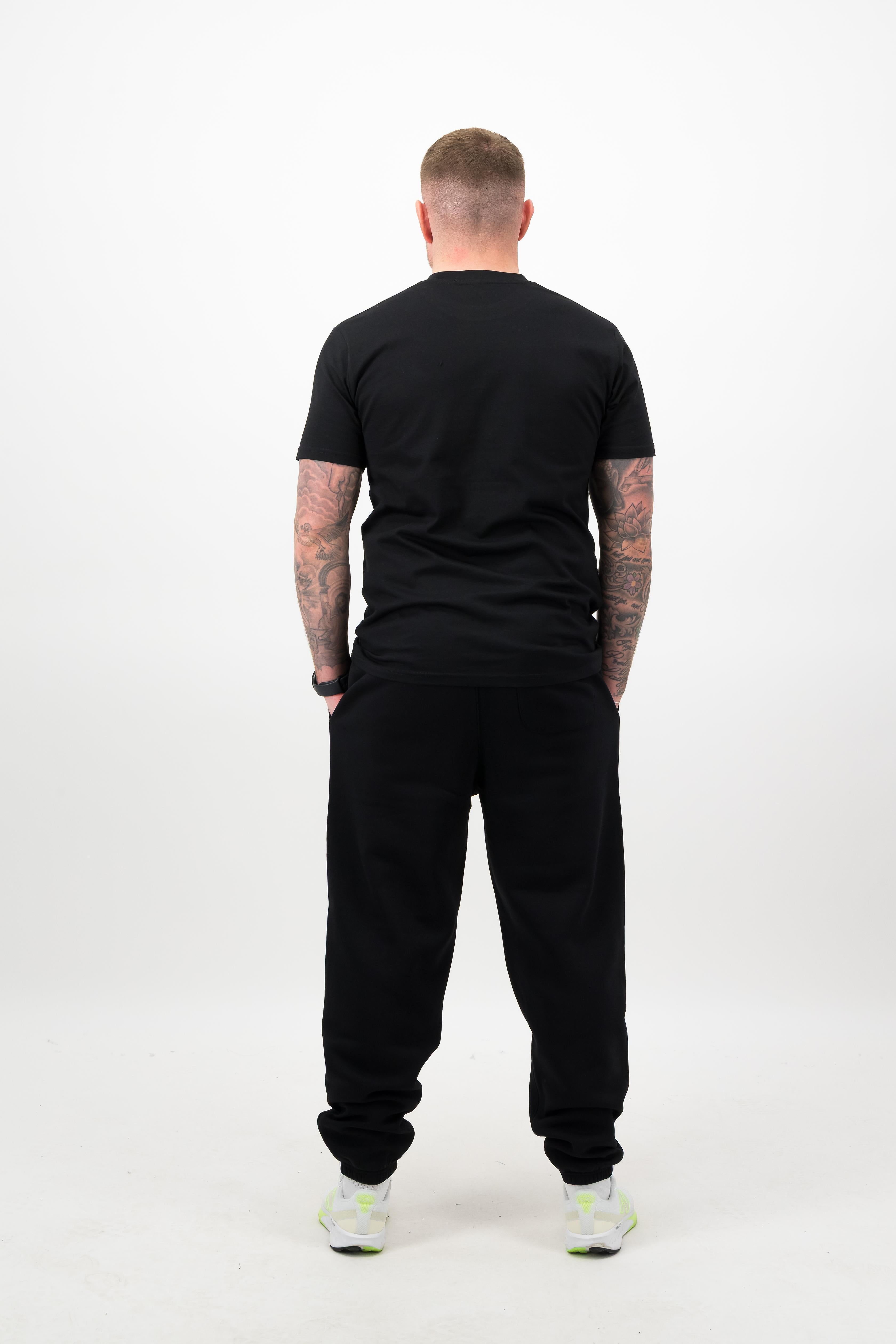 Person wearing a Concept Padel black rebound tee standing with back to camera showing the clean back silhouette, styled with black joggers and trainers against a white background