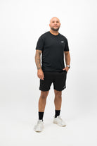 Person wearing a Concept Padel black performance tee standing facing forward, styled with dark shorts and trainers against a white background