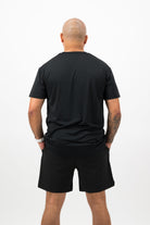 Person wearing Concept Padel black performance shorts standing with back to camera showing the clean back silhouette, styled with black tee and trainers against a white background