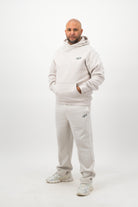 Man wearing Concept Padel bone sweatpants standing side on with one hand in pocket, paired with a matching sweatshirt and trainers against a white background