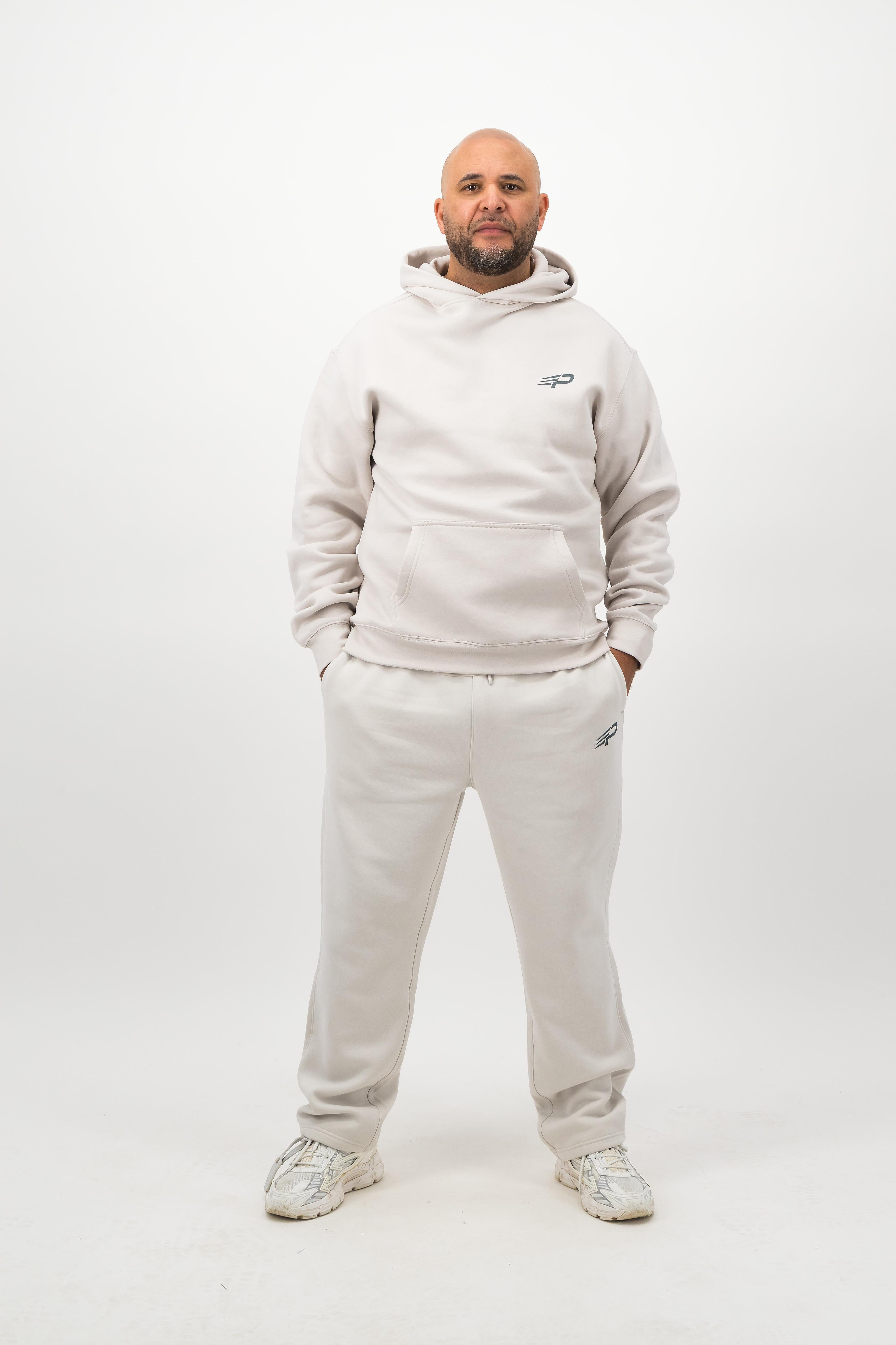 Man wearing Concept Padel bone sweatpants standing facing forward with hands in pockets, styled with a matching sweatshirt and trainers against a white background