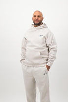 Man wearing Concept Padel bone sweatpants standing facing forward with hands in pockets, styled with a matching sweatshirt and trainers against a white background