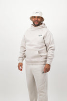 Man wearing Concept Padel bone sweatpants standing in a relaxed pose with arms by his sides, paired with a matching sweatshirt, bucket hat and trainers against a white background
