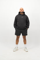 Person wearing a Concept Padel black faded hoodie standing facing forward, styled with black shorts and trainers against a white background