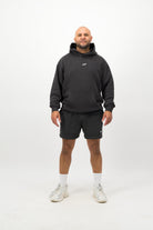 Person wearing a Concept Padel black faded hoodie standing facing forward, styled with black shorts and trainers against a white background
