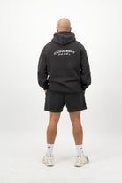 Person wearing a Concept Padel black faded hoodie standing with back to camera showing the back branding, styled with black shorts and trainers against a white background