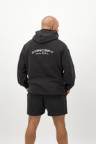 Person wearing a Concept Padel black faded hoodie standing with back to camera showing the back branding, styled with black shorts and trainers against a white background