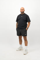Person wearing Concept Padel black faded sweat shorts standing facing forward, styled with black tee and trainers against a white background