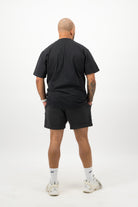 Person wearing a Concept Padel black faded tee standing with back to camera showing the clean back silhouette, styled with black shorts and trainers against a white background