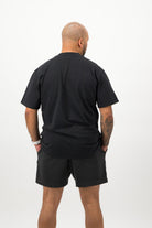 Person wearing a Concept Padel black faded tee standing with back to camera showing the clean back silhouette, styled with black shorts and trainers against a white background
