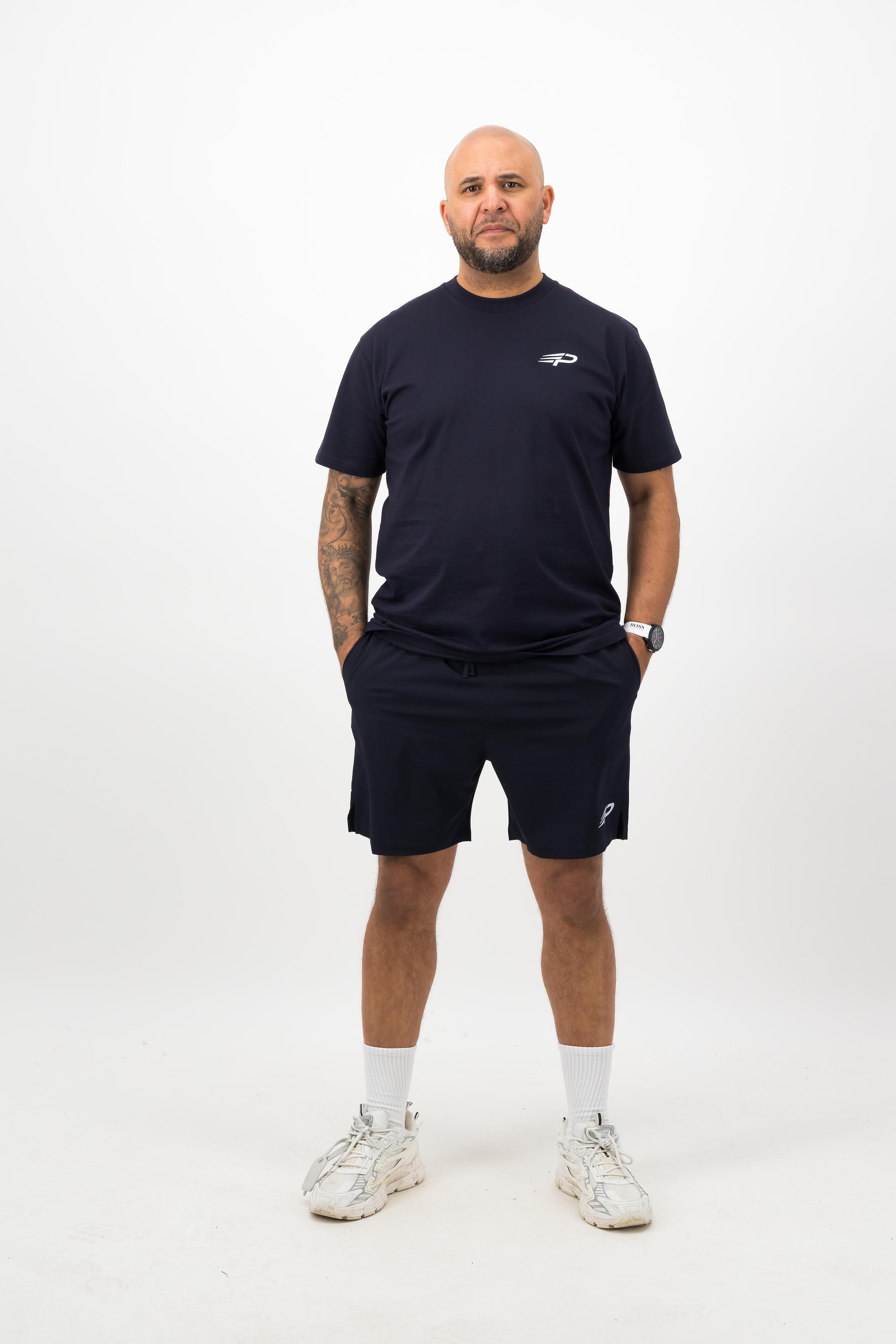 Person wearing a Concept Padel ink blue rebound tee standing facing forward, styled with matching shorts and trainers against a white background