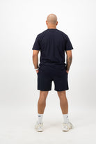 Person wearing a Concept Padel ink blue rebound tee standing with back to camera showing the clean back silhouette, styled with matching shorts and trainers against a white background