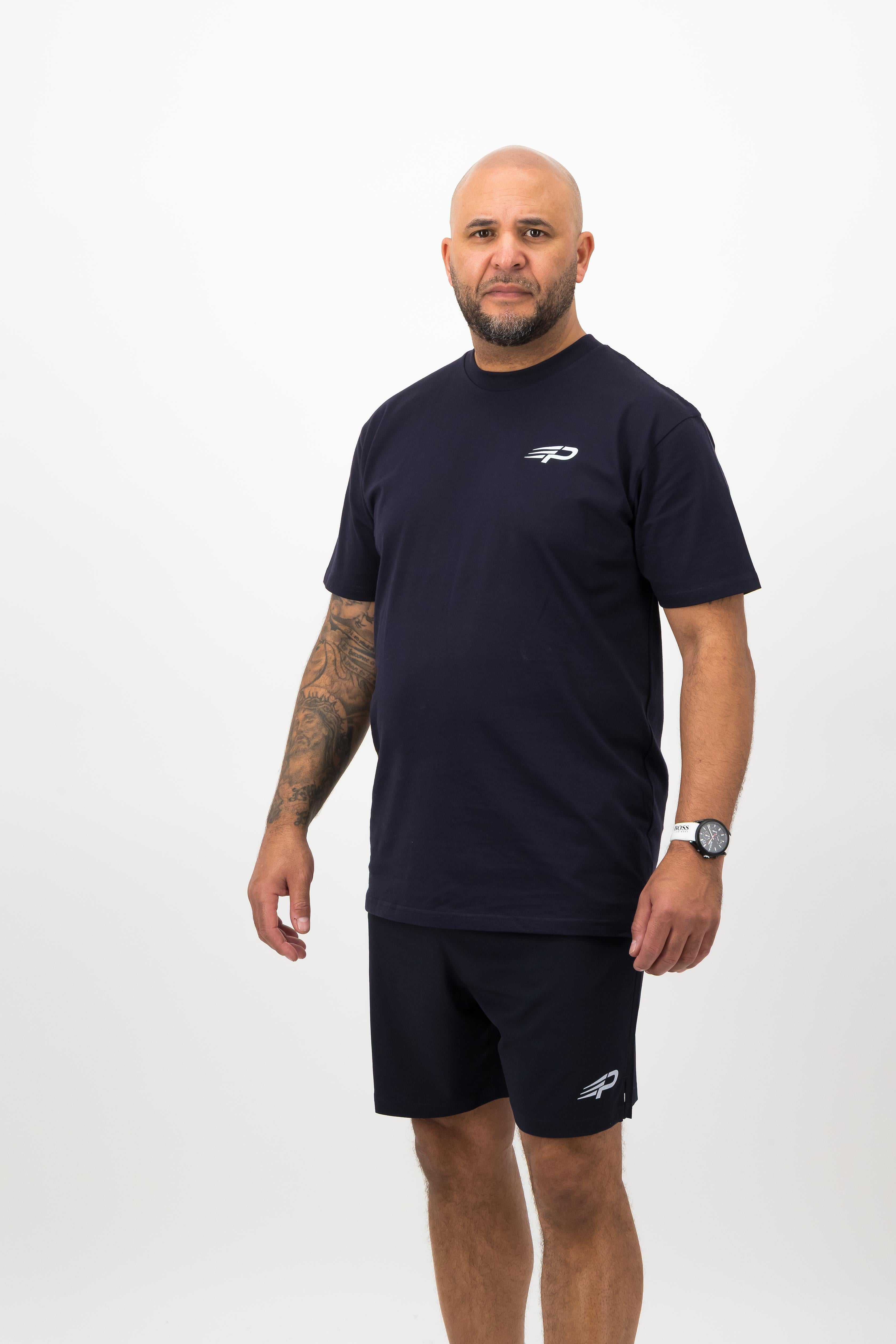 Person wearing a Concept Padel ink blue rebound tee standing facing forward, styled with matching shorts and trainers against a white background