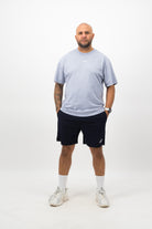 Person wearing a Concept Padel powder faded tee standing facing forward, styled with dark shorts and trainers against a white background