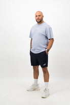 Person wearing a Concept Padel powder faded tee standing side on, paired with dark shorts and trainers against a white background