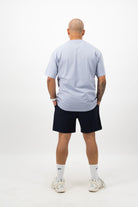 Person wearing a Concept Padel powder faded tee standing with back to camera showing the clean back silhouette, styled with dark shorts and trainers against a white background