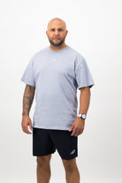 Person wearing a Concept Padel powder faded tee standing facing forward, styled with dark shorts and trainers against a white background