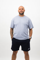 Person wearing a Concept Padel powder faded tee standing facing forward, styled with dark shorts and trainers against a white background