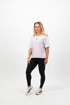 Woman wearing a Concept Padel orchid court tee standing facing forward with arms relaxed, styled with black shorts and trainers against a white background