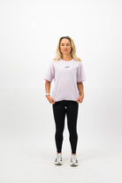 Woman wearing a Concept Padel orchid court tee standing facing forward with arms relaxed, styled with black shorts and trainers against a white background
