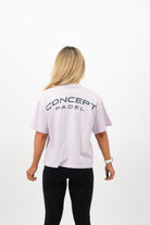 Close‑up of the Concept Padel logo on the orchid court tee worn by a woman against a white background