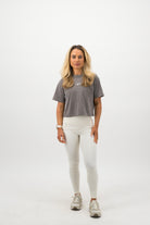 Woman wearing a Concept Padel grey faded crop tee standing facing forward, styled with white leggings and trainers against a white background