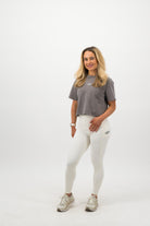 Woman wearing a Concept Padel grey faded crop tee standing facing forward, styled with white leggings and trainers against a white background