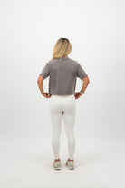 Woman wearing a Concept Padel grey faded crop tee standing with back to camera showing the clean back silhouette, styled with white leggings and trainers against a white background