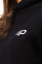 Close‑up of the Concept Padel logo on the black serve hoodie worn by a woman against a white background