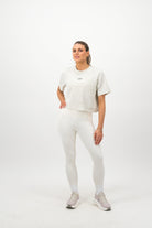 Woman wearing a Concept Padel bone faded crop tee standing facing forward, styled with white leggings and trainers against a white background