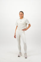 Woman wearing a Concept Padel bone faded crop tee standing facing forward, styled with white leggings and trainers against a white background