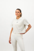 Woman wearing a Concept Padel bone faded crop tee standing facing forward, styled with white leggings and trainers against a white background