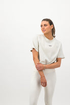 Woman wearing a Concept Padel bone faded crop tee standing side on, paired with white leggings and trainers against a white background