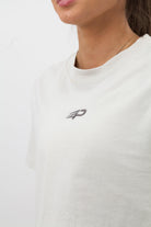 Close‑up of the embroidered Concept Padel logo on the bone faded crop tee worn by a woman against a white background