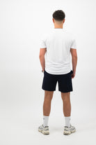 Person wearing a Concept Padel white performance tee standing with back to camera showing the clean back silhouette, styled with dark shorts and trainers against a white background