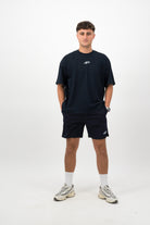 Person wearing Concept Padel ink blue performance shorts standing facing forward, styled with ink blue tee and trainers against a white background