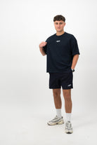 Person wearing Concept Padel ink blue performance shorts standing facing forward, styled with ink blue tee and trainers against a white background
