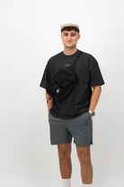Man wearing black Concept Padel body belt bag styled with oversized tee and grey shorts