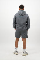 Person wearing a Concept Padel shadow rebound hoodie standing with back to camera showing the back branding, styled with grey shorts and trainers against a white background