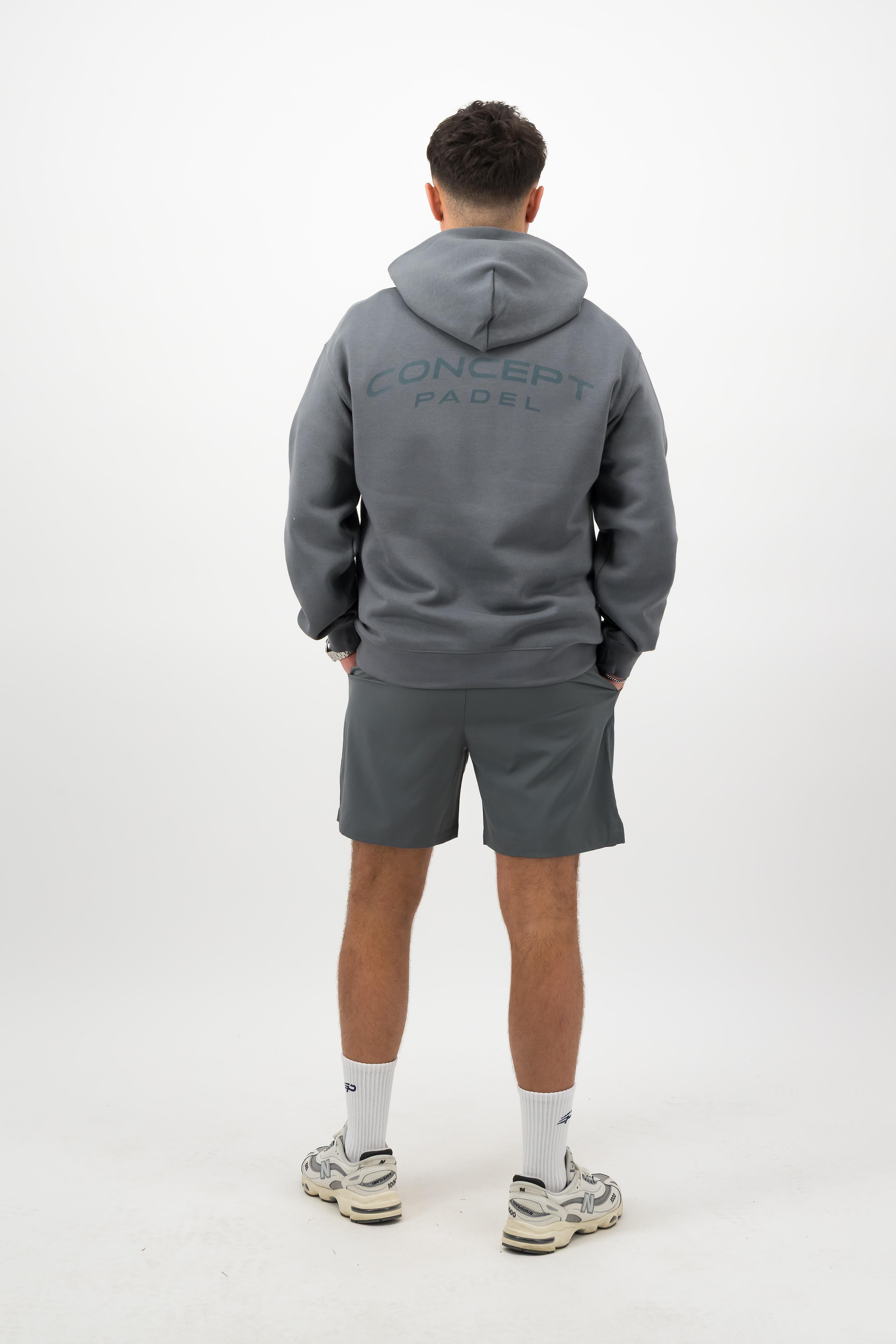 Person wearing a Concept Padel shadow rebound hoodie standing with back to camera showing the back branding, styled with grey shorts and trainers against a white background
