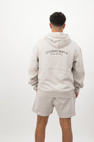 Person wearing a Concept Padel bone faded hoodie standing with back to camera showing the back branding, styled with matching shorts and trainers against a white background